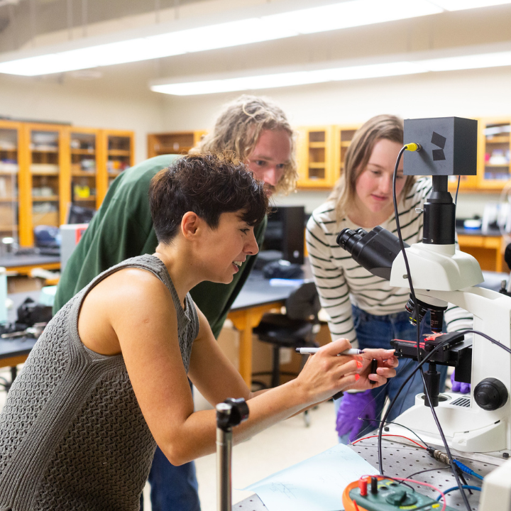 students and professor examining a microscope